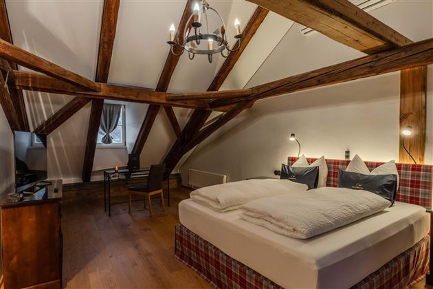 A cozy bedroom with a large double bed and a warm wooden ceiling. The room is bright and modernly furnished, ideal for a relaxing stay.
