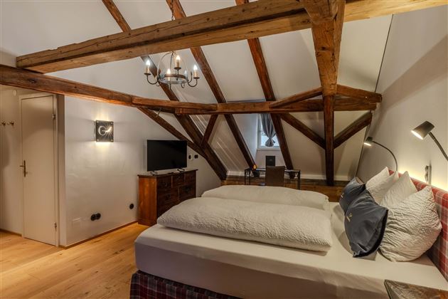 A cozy bedroom with wooden beamed ceilings. The room is well equipped with a double bed, a desk, and a television.