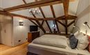 A cozy bedroom with wooden beamed ceilings. The room is well equipped with a double bed, a desk, and a television.