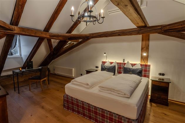 A cozy bedroom with wooden ceilings and a double bed. There is a desk and stylish lighting.