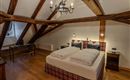 A cozy bedroom with wooden ceilings and a double bed. There is a desk and stylish lighting.