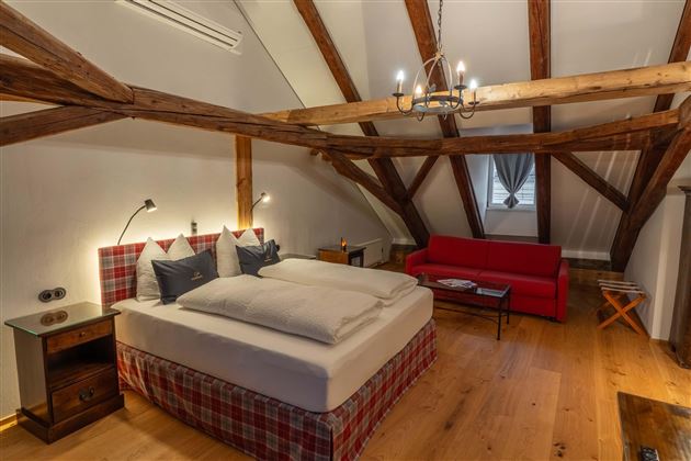 A cozy bedroom with a large bed and wooden ceilings. In the room, there is a red sofa and wooden furniture.