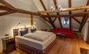 A cozy bedroom with a large bed and wooden ceilings. In the room, there is a red sofa and wooden furniture.