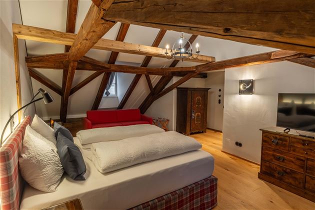 A cozy bedroom with wooden beams and a large bed. The decor is rustic and inviting, featuring a television and a dresser.