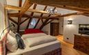 A cozy bedroom with wooden beams and a large bed. The decor is rustic and inviting, featuring a television and a dresser.