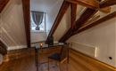A cozy attic room with visible wooden beams. There is a desk with a chair at the window.
