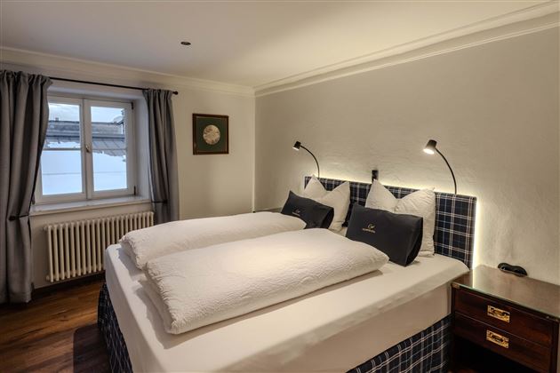 A cozy bedroom with two beds and modern reading lamps. The window lets in plenty of daylight and offers a view outside.