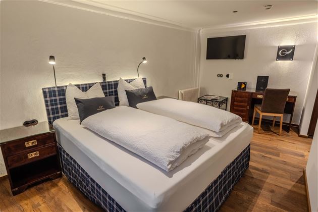 A modern hotel room with a large double bed and wooden floor. There is a desk and a television on the wall.