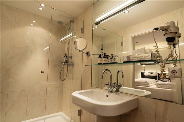 A modern bathroom with a glass shower cabin and sink. Skincare products are arranged on a shelf.
