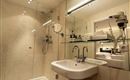 A modern bathroom with a glass shower cabin and sink. Skincare products are arranged on a shelf.