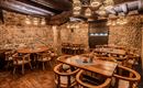 A cozy restaurant with wooden tables and chairs. The walls are made of stones and decorative lamps hang from the ceiling.