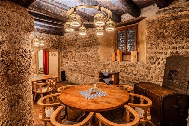 A rustic room with stone walls and a large wooden table in the center. The lighting is complemented by a modern lamp above the table.