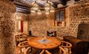 A rustic room with stone walls and a large wooden table in the center. The lighting is complemented by a modern lamp above the table.