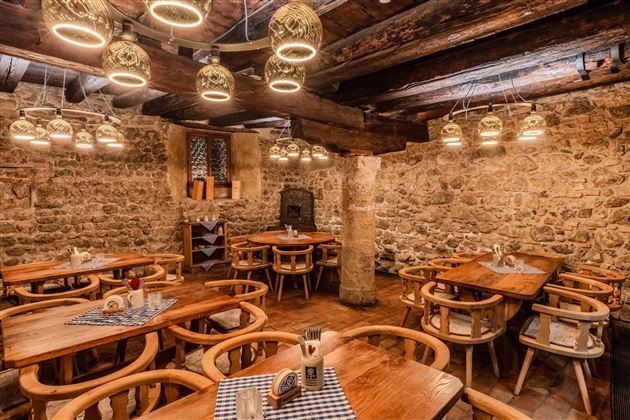 A cozy restaurant with wooden tables and chairs. The walls are made of stone, and the lighting is warm and inviting.