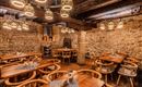 A cozy restaurant with wooden tables and chairs. The walls are made of stone, and the lighting is warm and inviting.