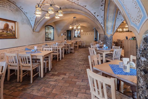 A cozy restaurant with wooden tables and chairs. The walls are designed with decorative elements and an arch.