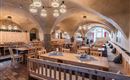 A cozy restaurant with wooden furniture and a warm atmosphere. Large tables and appealing lighting enhance the inviting ambiance.
