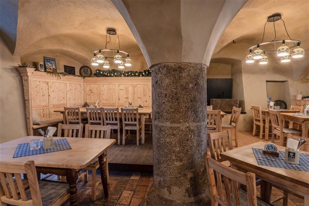A cozy restaurant with wooden tables and chairs. The walls are designed with stone and wood, and there are warm light sources.