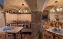 A cozy restaurant with wooden tables and chairs. The walls are designed with stone and wood, and there are warm light sources.