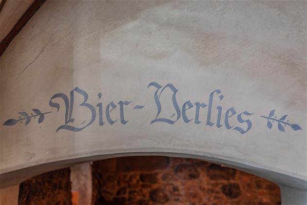 A decorative sign with the inscription "Beer Dungeon". It is located on a wall and conveys a rustic atmosphere.