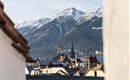 A picturesque view of the town with snow-covered mountains in the background. The roofs of the buildings are clearly visible and convey a cozy, alpine atmosphere.