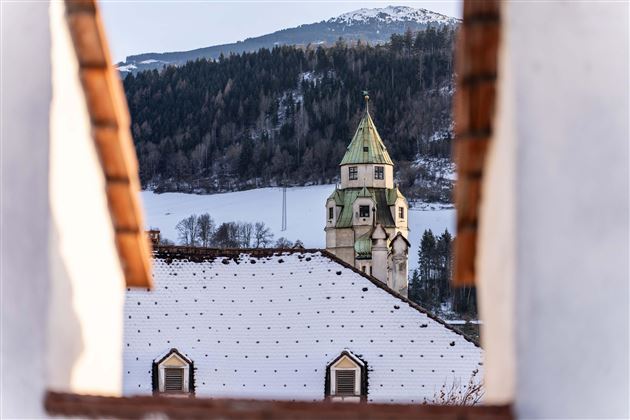 A beautiful view of a church tower surrounded by snow-covered roofs. In the background, mountains and a clear sky can be seen.