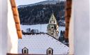 A beautiful view of a church tower surrounded by snow-covered roofs. In the background, mountains and a clear sky can be seen.