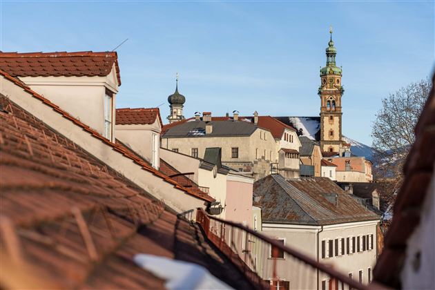 A view over the roofs of a city with historical buildings and a distinctive tower. The sky is clear and blue.