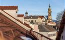 A view over the roofs of a city with historical buildings and a distinctive tower. The sky is clear and blue.