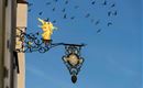 A golden angel on a historical shield under a clear blue sky. Above the shield, many birds are flying.