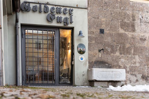 A shop named "Golden Eugl" is visible. The facade is plain and modern, with a wrought-iron gate and a stone wall in the background.