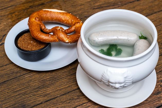 A Bavarian meal with a pretzel and white sausages in a bowl. There is sweet mustard in a small dish.