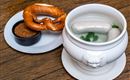 A Bavarian meal with a pretzel and white sausages in a bowl. There is sweet mustard in a small dish.