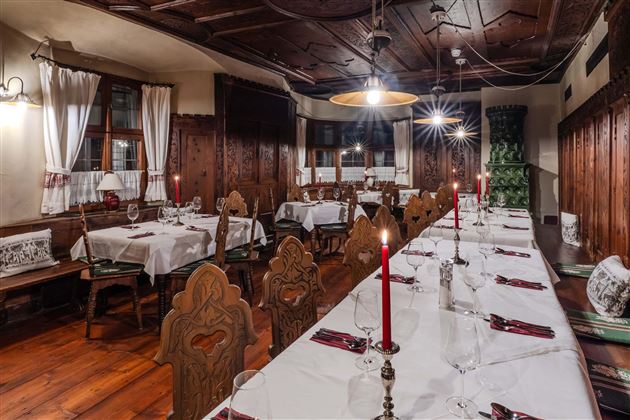 A cozy restaurant with wooden furniture and elegant table decoration. The tables are set for a festive meal and adorned with red candles.