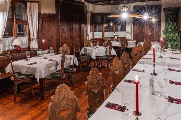 A cozy restaurant with elegant wooden furniture and tablecloths. Red candles create a warm atmosphere.