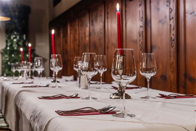 A festively laid table with glasses and red candles. The background features rustic wood paneling.