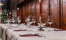 A festively laid table with glasses and red candles. The background features rustic wood paneling.