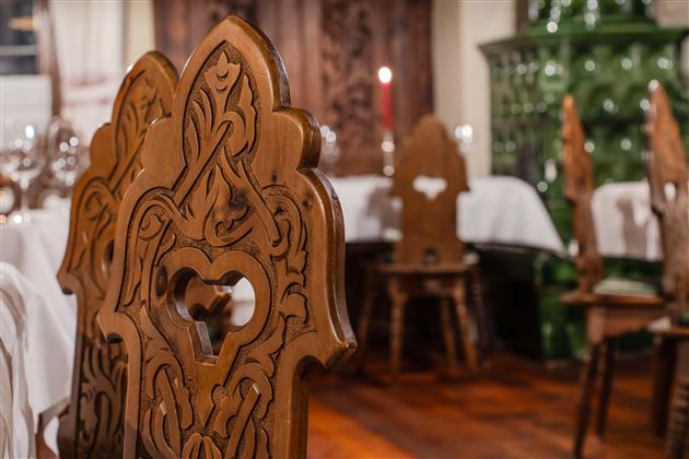 A traditional restaurant with intricately carved wooden chairs. In the background, you can see a cozy atmosphere with laid tables.