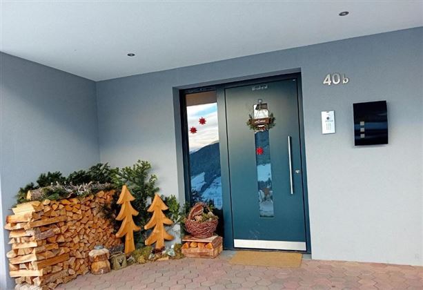 Een moderne voordeur met een feestelijke decoratie. Naast de deur staat een houtstapel en kerstboomfiguren.