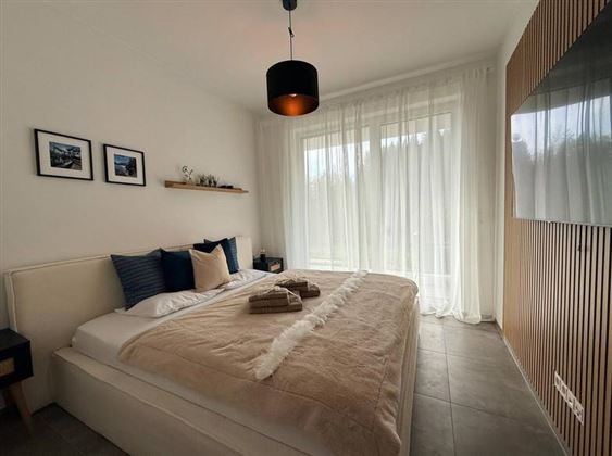 Ein modernes Schlafzimmer mit einem großen Bett und sanften Farbtönen. Große Fenster lassen viel Licht herein und sorgen für eine helle, freundliche Atmosphäre.