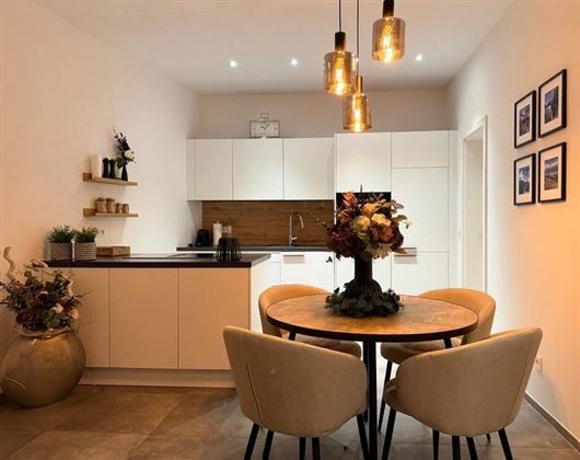 Eine moderne Küche mit einem runden Esstisch und stylischen Stühlen. Dekorative Elemente und eine angenehme Beleuchtung schaffen eine einladende Atmosphäre.