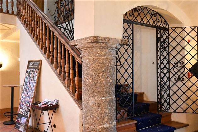 A staircase with a wooden railing and a closed door. In the foreground stands a stone column pillar.