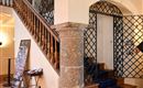 A staircase with a wooden railing and a closed door. In the foreground stands a stone column pillar.