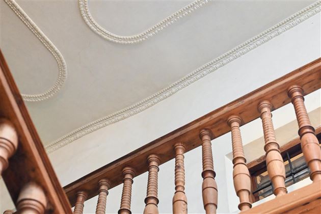 A staircase with wooden railings and ornate ceiling decorations. The picture shows the view upward towards the ceiling.