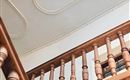 A staircase with wooden railings and ornate ceiling decorations. The picture shows the view upward towards the ceiling.