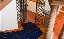 A staircase with a blue carpet runner leads downwards. In the background, there are grill doors and light walls visible.