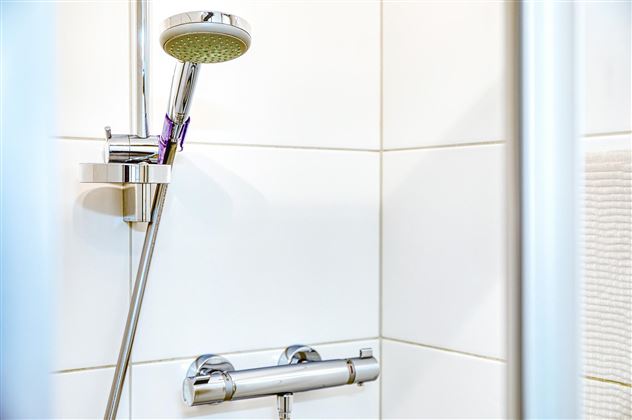Une situation de douche avec une douchette moderne et des carreaux blancs. L'image montre la douche dans une salle de bain lumineuse et propre.