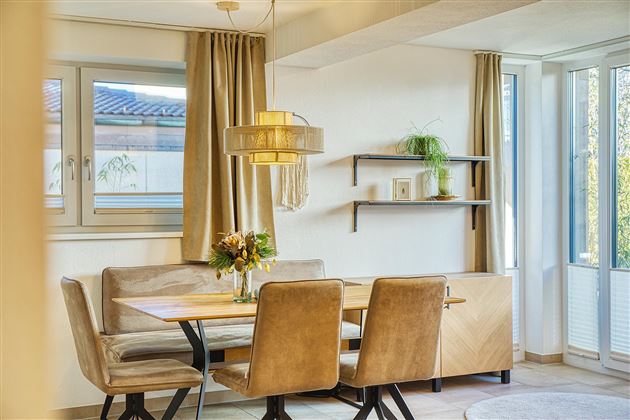 Une salle à manger accueillante avec un plateau en bois et des chaises élégantes. De grandes fenêtres laissent entrer beaucoup de lumière naturelle.