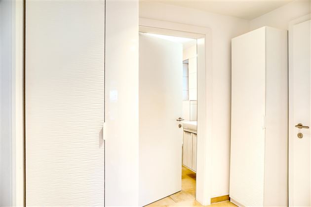 Un couloir lumineux avec des murs et des portes blancs.  
Sur le côté gauche se trouve une armoire et sur le côté droit une autre armoire.