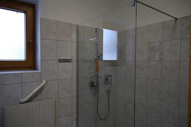 Eine moderne Dusche mit transparenten Glastüren und gefliesten Wänden. Das Badezimmer hat ein Fenster, das Tageslicht hereinlässt.
